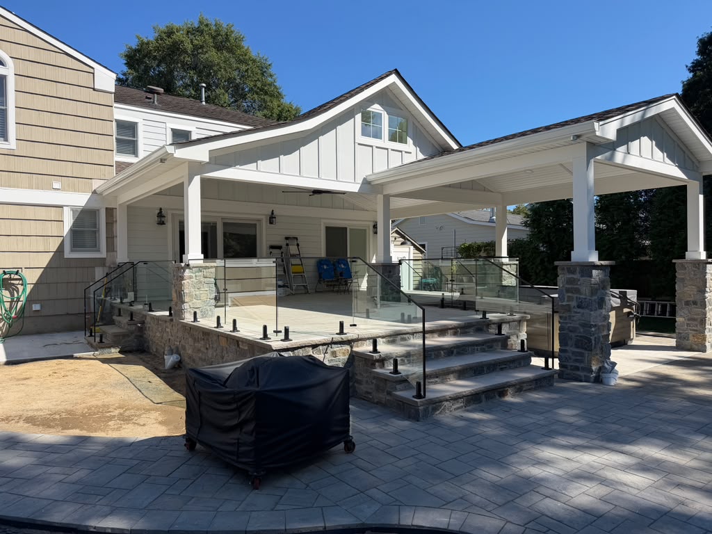 Frameless glass railing with black standoffs around a covered stone patio and steps
