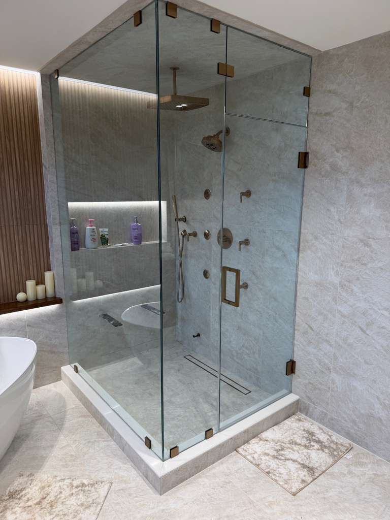 Frameless corner glass shower enclosure with brushed bronze hardware and marble tile
